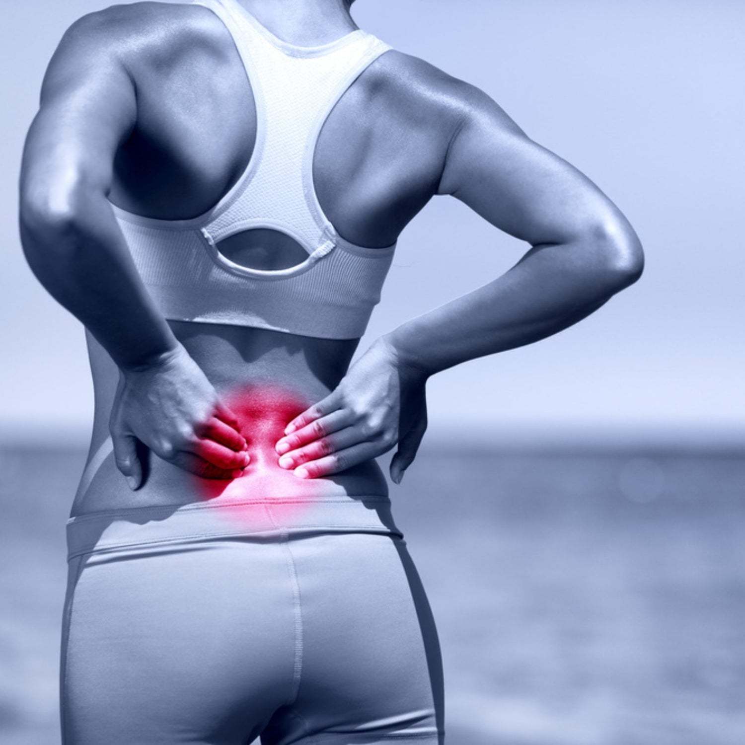 a girl holding her back wearing athletic clothing on a beach