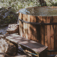 A cheap, at home cold plunge tub. It is in wooden form and has a nature backdrop.